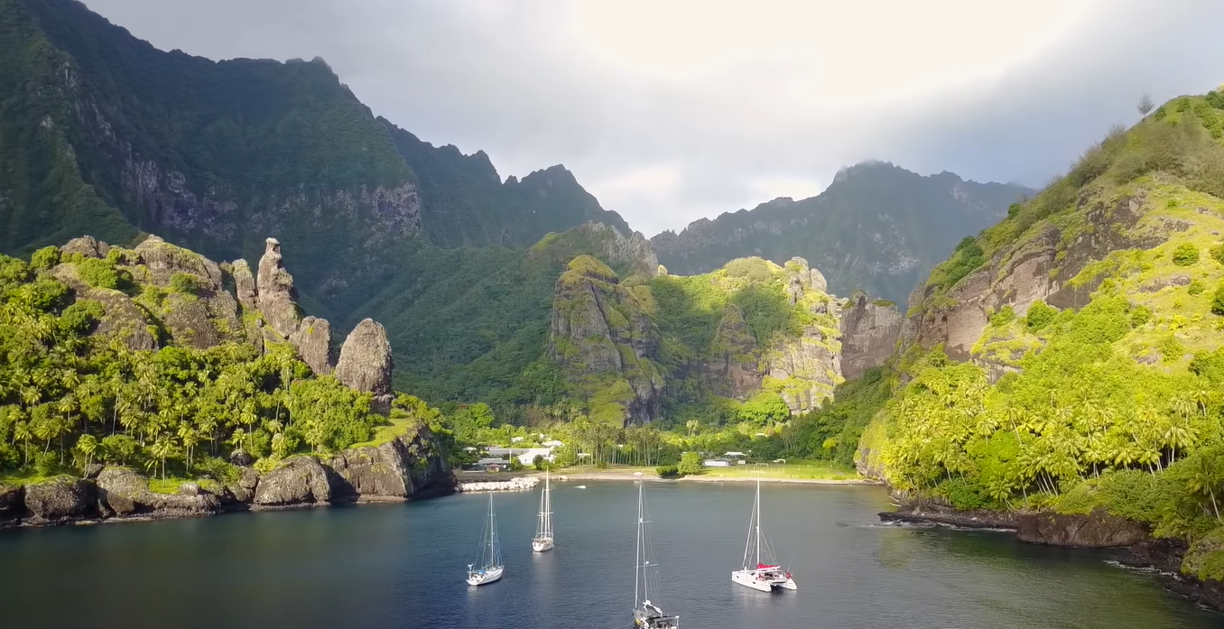Four boats sailing towards Marquesas Islands, with its rocky landscape littered with trees