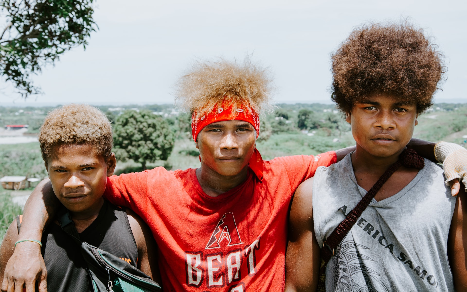 Three male teenagers in Solomon Islands, with the middle one’s arms placed over the shoulders of the other two