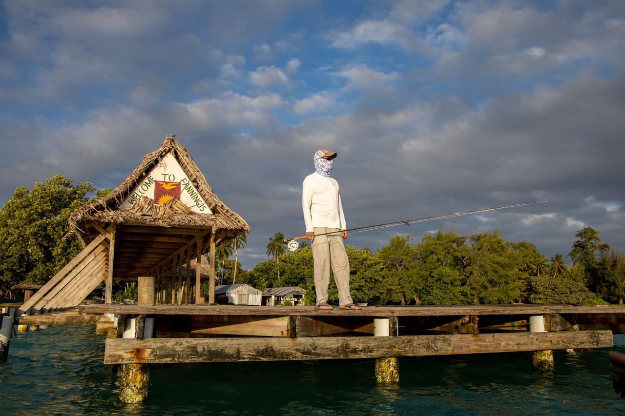 Male holding a long rod and standing on the edge of a wooden platform by the waters of Fanning Island