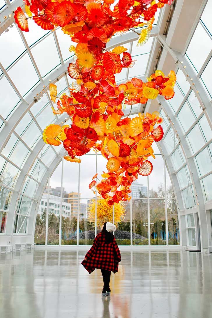 A woman walking inside the Chihuly Garden And Glass and looking at the big orange flowers