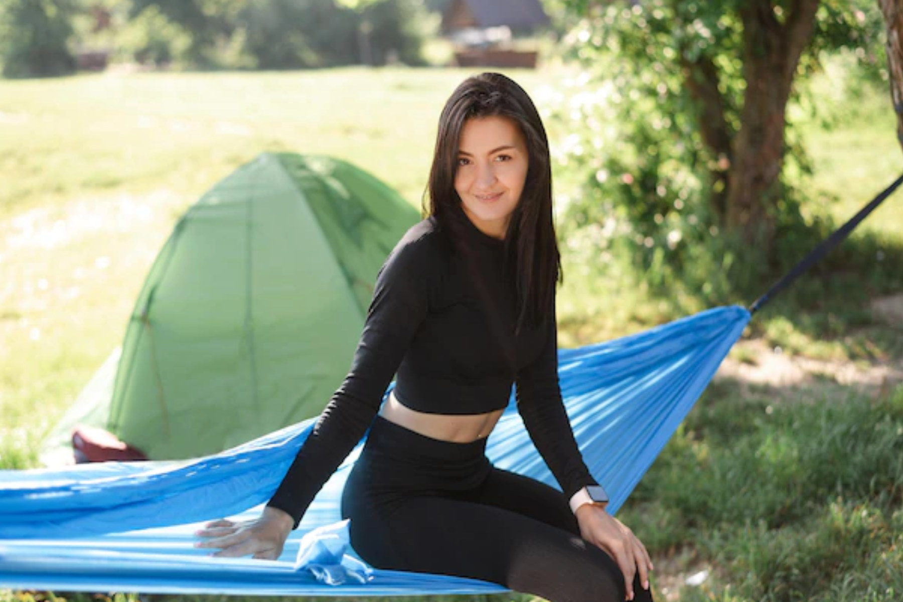 A woman is seated on a blue swing in front of her camping tent