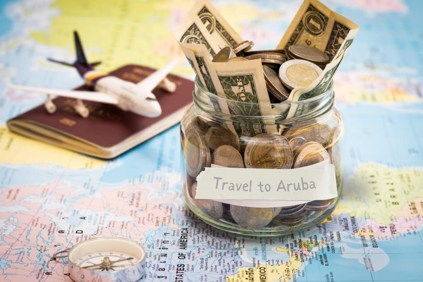 A little jar glass with money and the label "Travel to Aruba" on top of the map, as well as a miniature plane on top of the passport