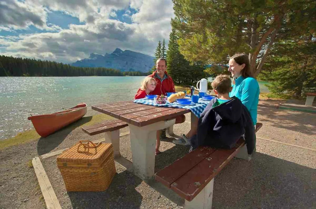 A family having a picnic on a wooden table and bench in Lake Louise Campgrounds