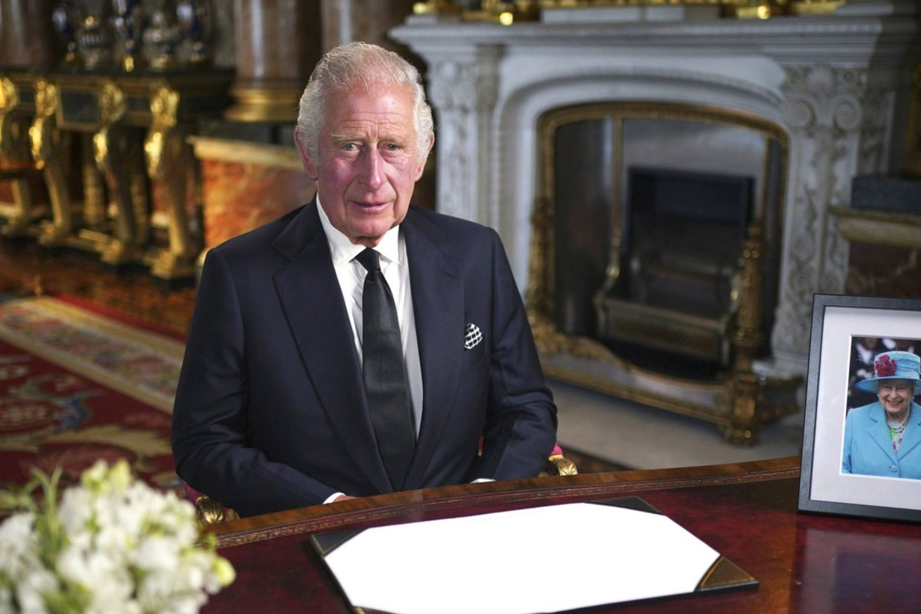 King Charles III seated at a table with a photograph of his late mother Queen Elizabeth