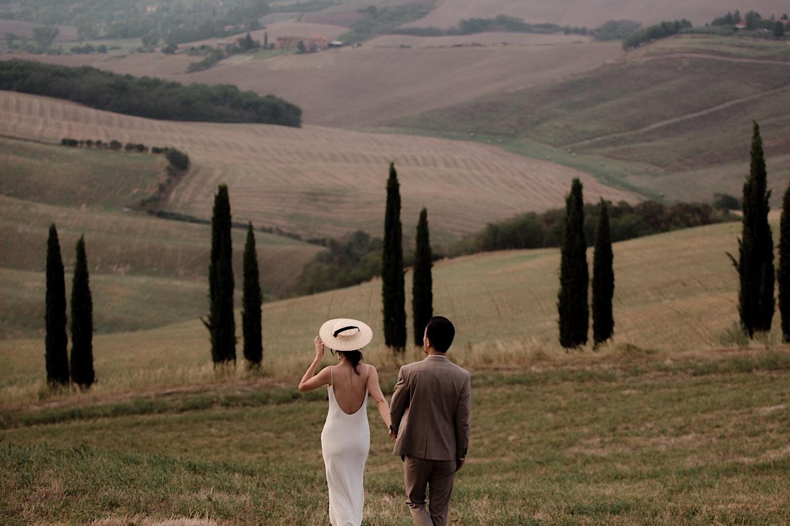 A couple holding hands walking in a vast field in Tuscany Italy