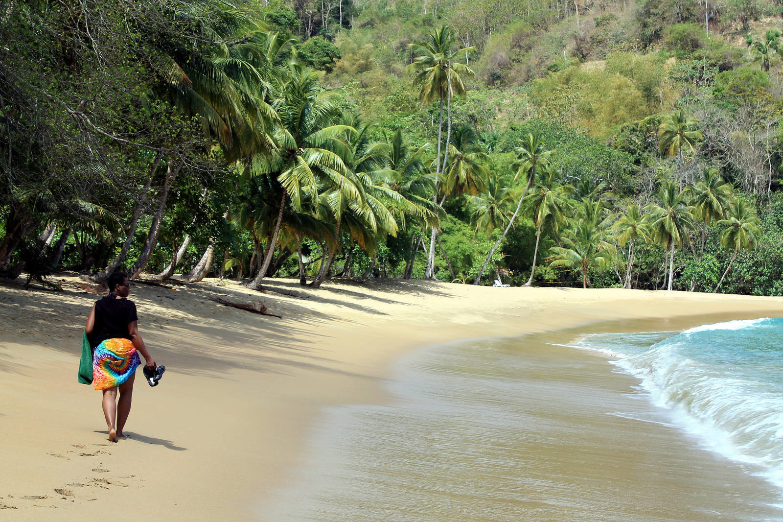 A woman walking on the shore of a beach in Trinidad And Tobago while holding her footwear