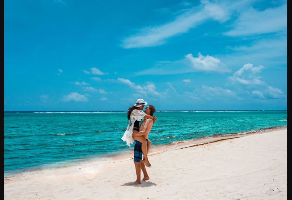 A man carrying a woman on the shore of a beach in the Grand Cayman