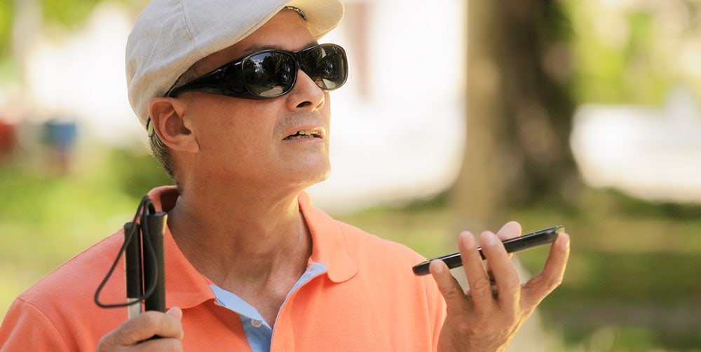 A blind man wearing sunglasses, holding a cane and a smartphone.
