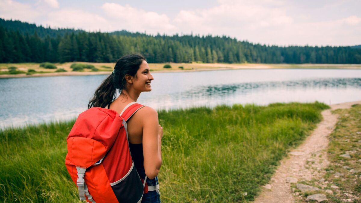 A woman carrying a red backpack standing before a lake