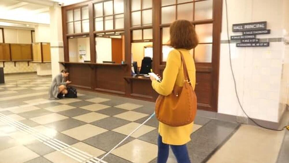 A blind woman with her cane, smartphone and shoulder bag walking in an office.