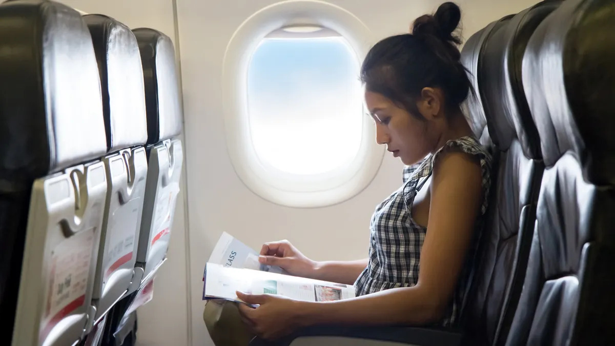 Woman on a plane near window seat, reading a magazine.